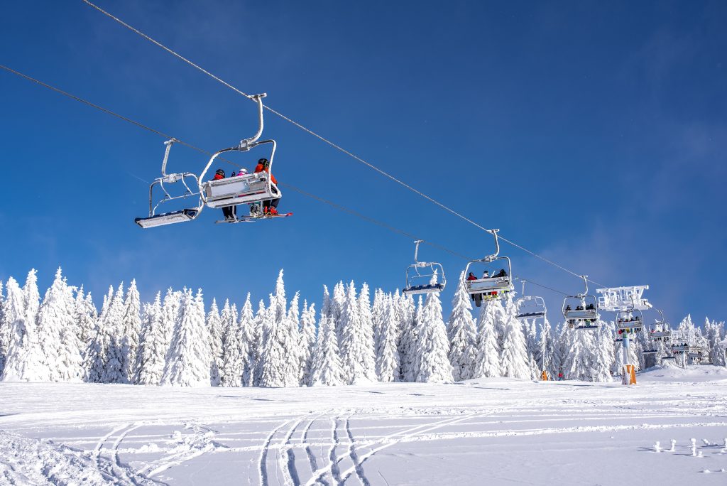 A low angle shot of skiers on a ski lift at a mountain resort with the sky and mountains in the background
